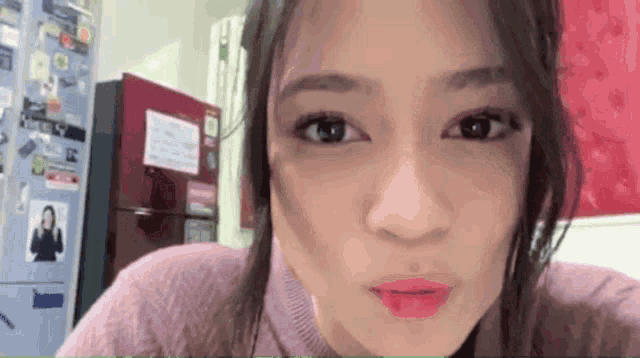 a woman in a pink sweater is making a funny face in front of a red refrigerator .