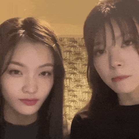 two young women are standing next to each other and looking at the camera with a patterned wall in the background