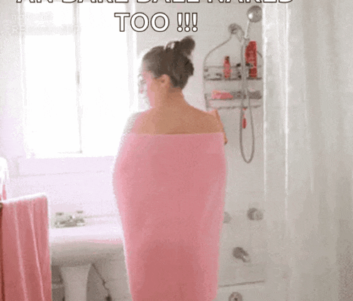 a woman wrapped in a pink towel standing in a bathroom .