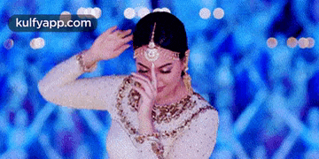a woman in a white dress is dancing in front of a blue background with the words kulfyapp.com on the bottom .