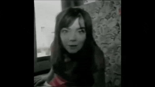 a black and white photo of a person standing in a room with a light coming through the window .