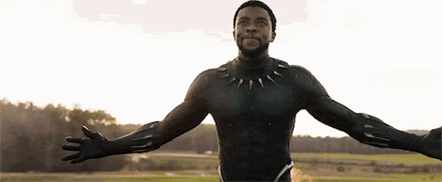a man in a black suit is standing with his arms outstretched in a field .