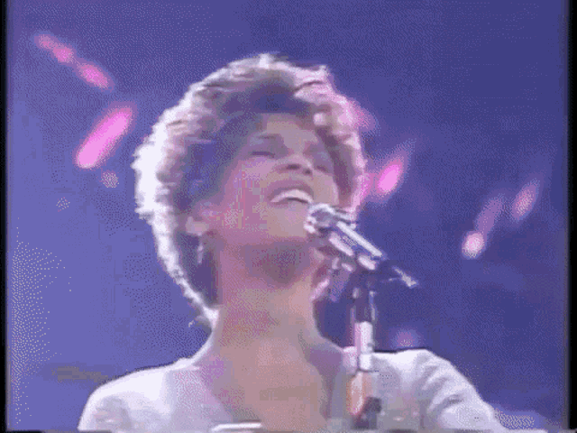 a woman is singing into a microphone on a stage in a dark room .