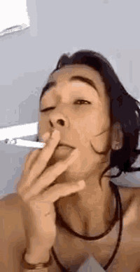a woman is smoking a cigarette while taking a selfie with her eyes closed .