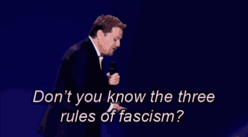 a man in a suit is holding a microphone and saying " don t you know the three rules of fascism "