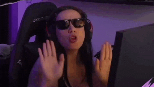 a woman wearing sunglasses and headphones is sitting in front of a computer screen covering her face with her hands .