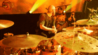a man playing drums in a dark room with a yellow background