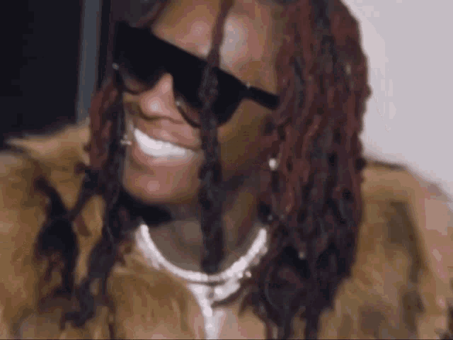a man wearing sunglasses and a fur coat is smiling