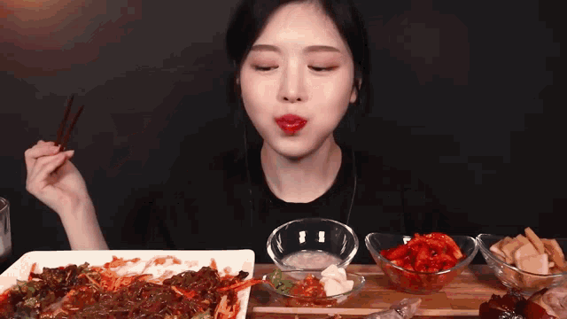 a woman is eating food with chopsticks while sitting at a table with bowls of food