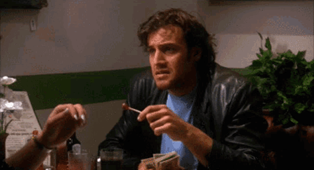 a man in a leather jacket is sitting at a table with a fork in his hand
