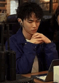 a young man wearing headphones is sitting at a table with his hands folded .