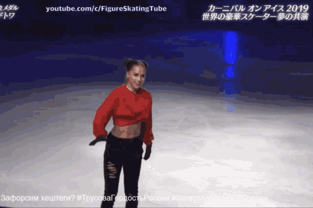 a woman in a red sweater and black pants is standing on a ice rink