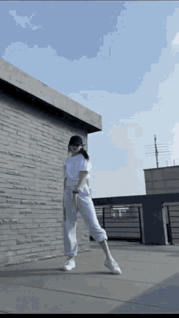 a woman wearing a white shirt and grey sweatpants is dancing on a rooftop
