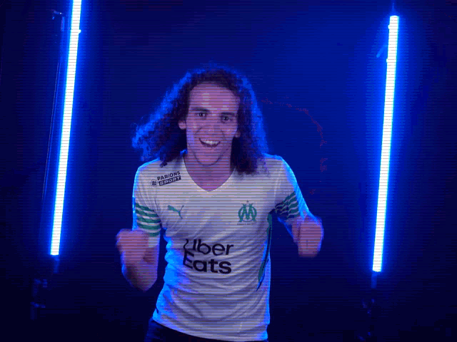 a man with curly hair wears a white shirt that says uber eats on it