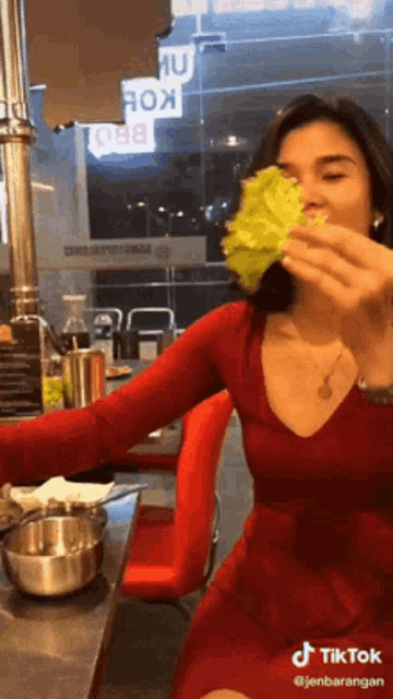 a woman in a red dress is eating a leaf of lettuce ..