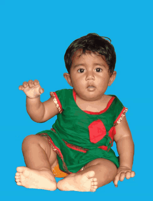 a baby in a green and red outfit is sitting on a blue surface