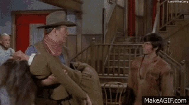 a man in a hat is standing in a room next to a man in a vest .