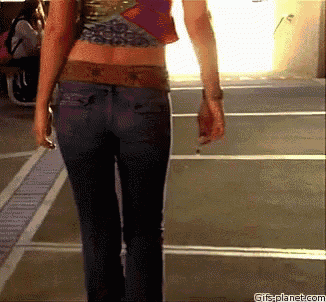 a woman wearing jeans and a crop top walks down a street with a gifsplanet.com watermark