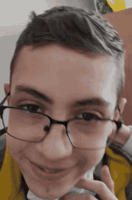 a young boy wearing glasses and a yellow jacket is smiling and holding a mask .