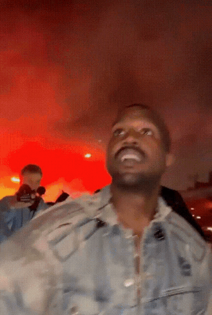a man in a denim jacket is smiling in front of a fire