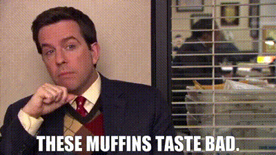 a man in a suit and tie is sitting in front of a window with blinds and says `` these muffins taste bad '' .