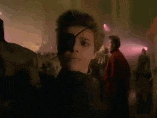 a man with a bandage on his eye is standing in a dark room with a crowd of people .