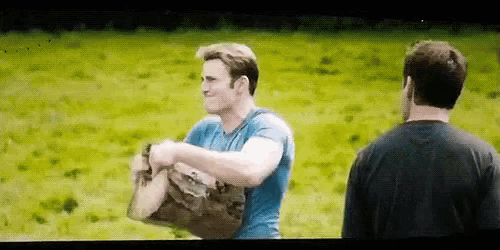 a man in a blue shirt is carrying a bag in a field while another man looks on .