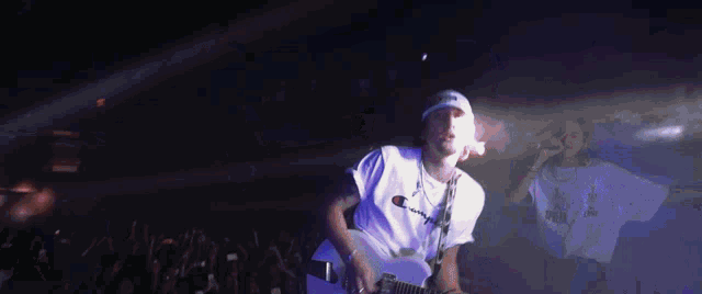 a man wearing a champion shirt is playing a guitar on stage