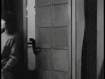 a black and white photo of a woman standing next to a door .