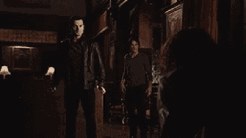 a man in a leather jacket is standing in a dark room next to a woman .