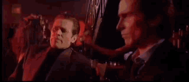 a man in a suit and tie is talking to another man in a dark room .