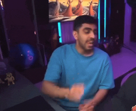 a man in a blue shirt is dancing in front of a purple wall