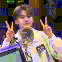 a young man is giving a peace sign in front of a microphone in a room .