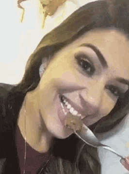 a woman is smiling while eating a piece of food with a spoon .