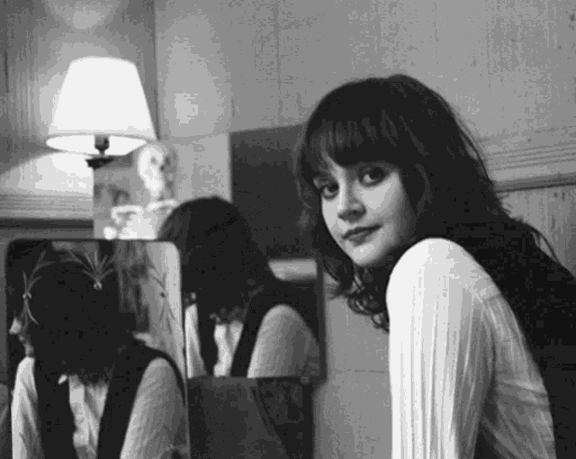 a black and white photo of a woman looking at herself in the mirror