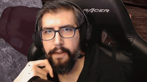 a man with glasses and a beard is sitting in a black racer chair