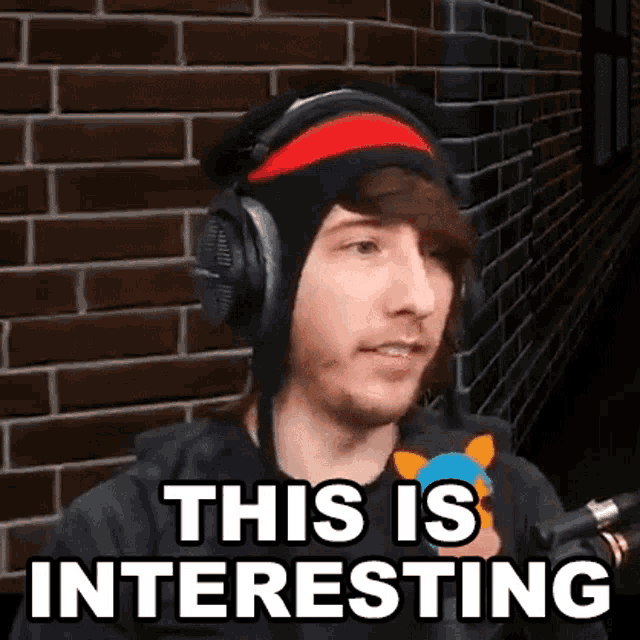 a man wearing headphones and a headband is standing in front of a brick wall and saying this is interesting .