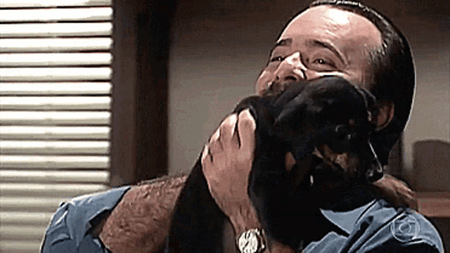 a man in a blue shirt is holding a small black dog in his arms