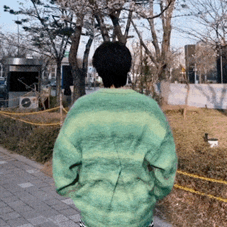 a person wearing a green sweater walking down a sidewalk