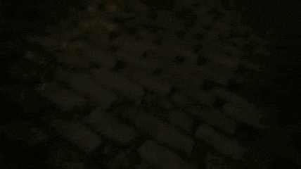 two robots are standing next to each other on a brick floor in a dark room .