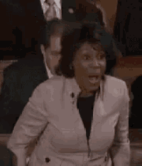a woman in a trench coat is sitting in a courtroom with a man in a suit behind her .