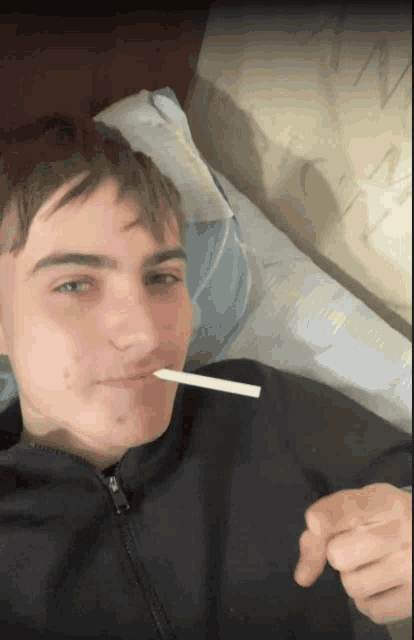 a young man is laying on a bed holding a cigarette in his mouth