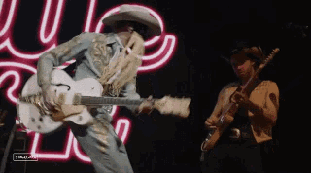 two men are playing guitars on stage in front of a neon sign .