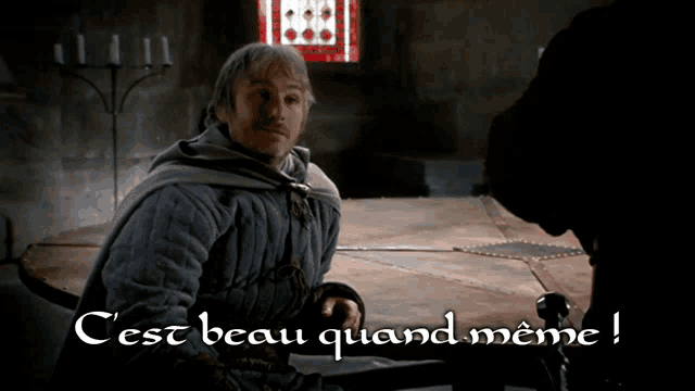 a man sitting at a table with the words " c'est beau quand meme " on the bottom