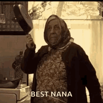 an elderly woman is holding a frying pan in a kitchen and says `` best nana '' .