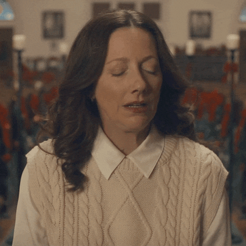 a woman with her eyes closed wearing a sweater vest and white shirt