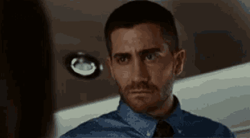 a man in a blue shirt and tie is looking at another man in a mirror .
