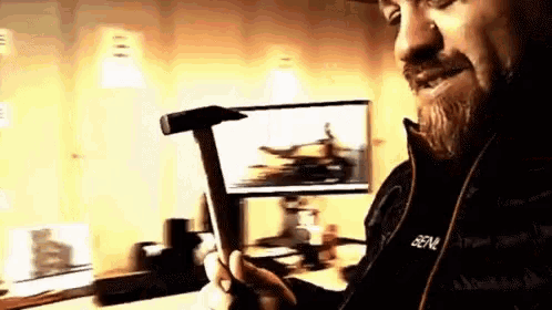 a man with a beard is holding a hammer in front of a computer