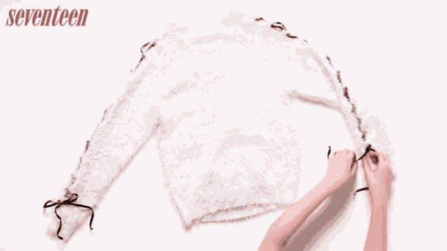 a woman is putting a necklace on a sweater and a pink skirt