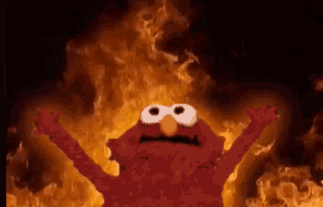 elmo from sesame street is standing in the middle of a fire .